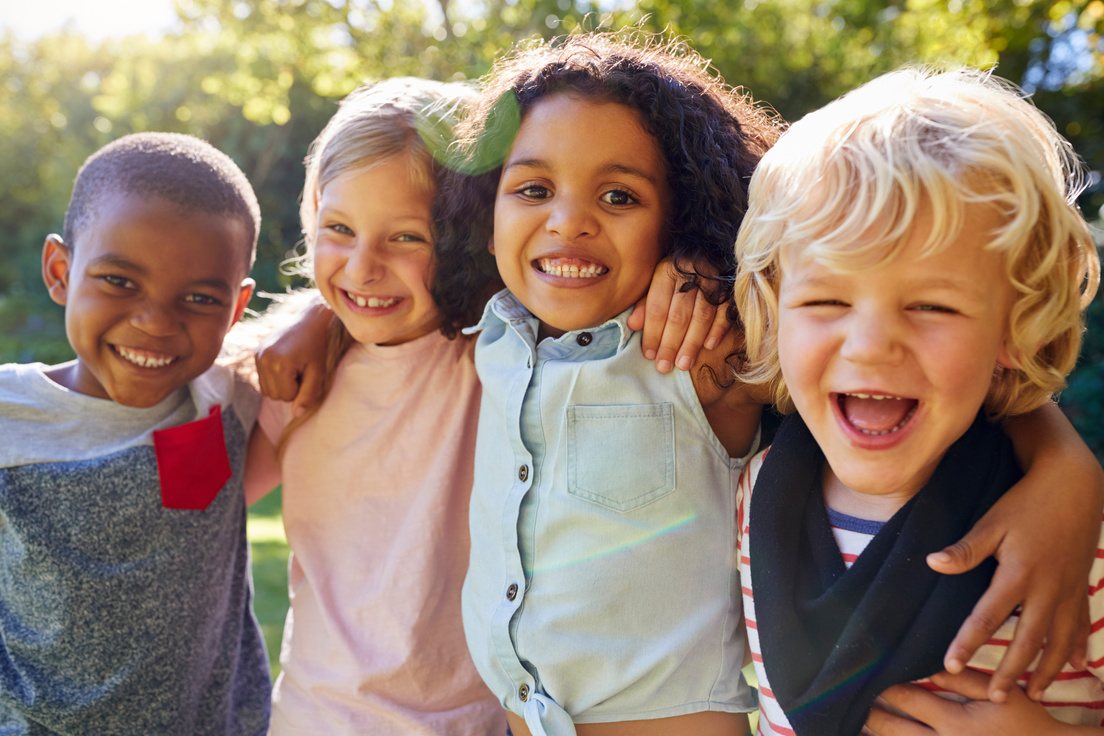 Vier Kinder haben die Arme umeinander gelegt und grinsen.